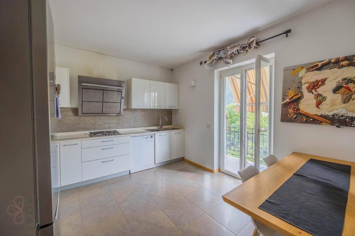Moderne weiße Küche mit Essbereich, Fliesenboden und direktem Zugang zum Balkon.