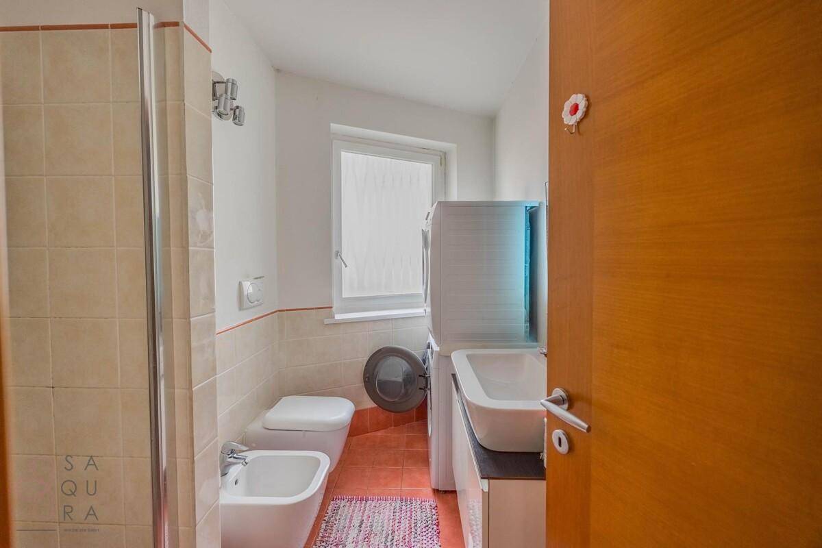 Praktisches Badezimmer mit Dusche, WC, Bidet und Waschmaschine, mit Fenster für Tageslicht.