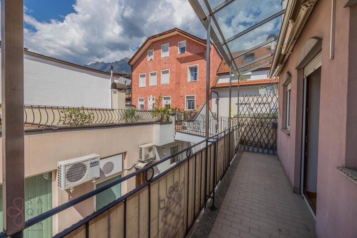Überdachter Balkon mit Metallgeländer und Ausblick auf die Nachbarschaft und Berge im Hintergrund.