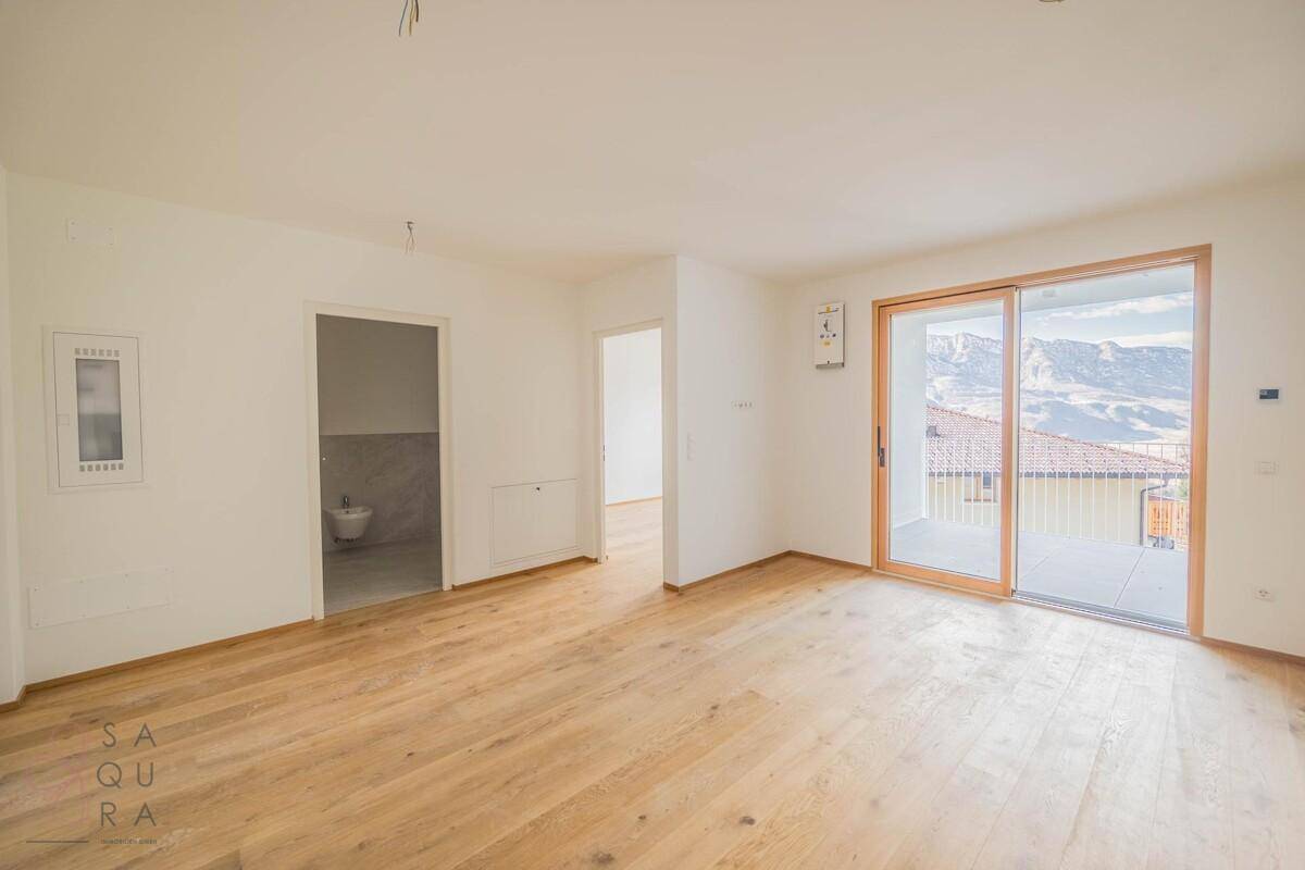 Heller Wohnraum mit Holzboden, Balkonzugang und Blick auf die Berge, angrenzend an ein Badezimmer.