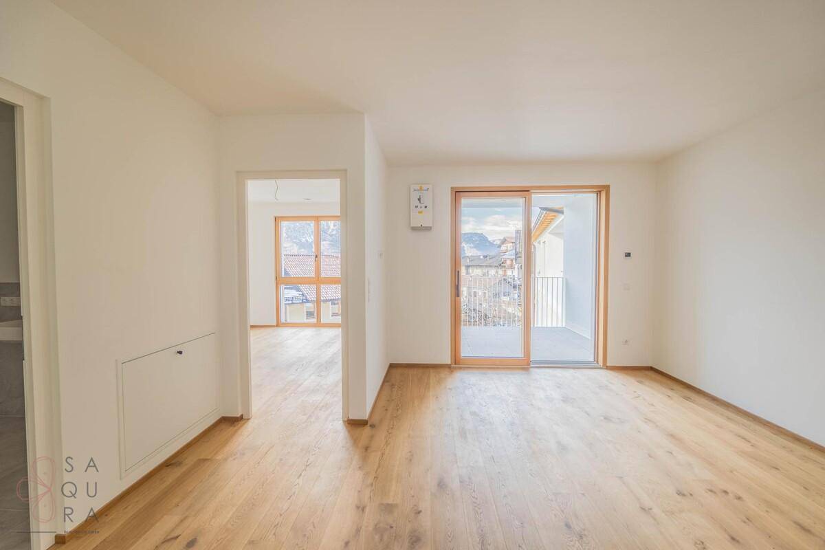 Geräumiger, unmöblierter Raum mit hellem Holzboden und Schiebetür zum Außenbereich.