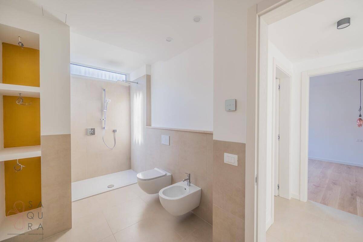 Modernes Badezimmer mit begehbarer Dusche, Bidet und beigefarbenen Fliesen.