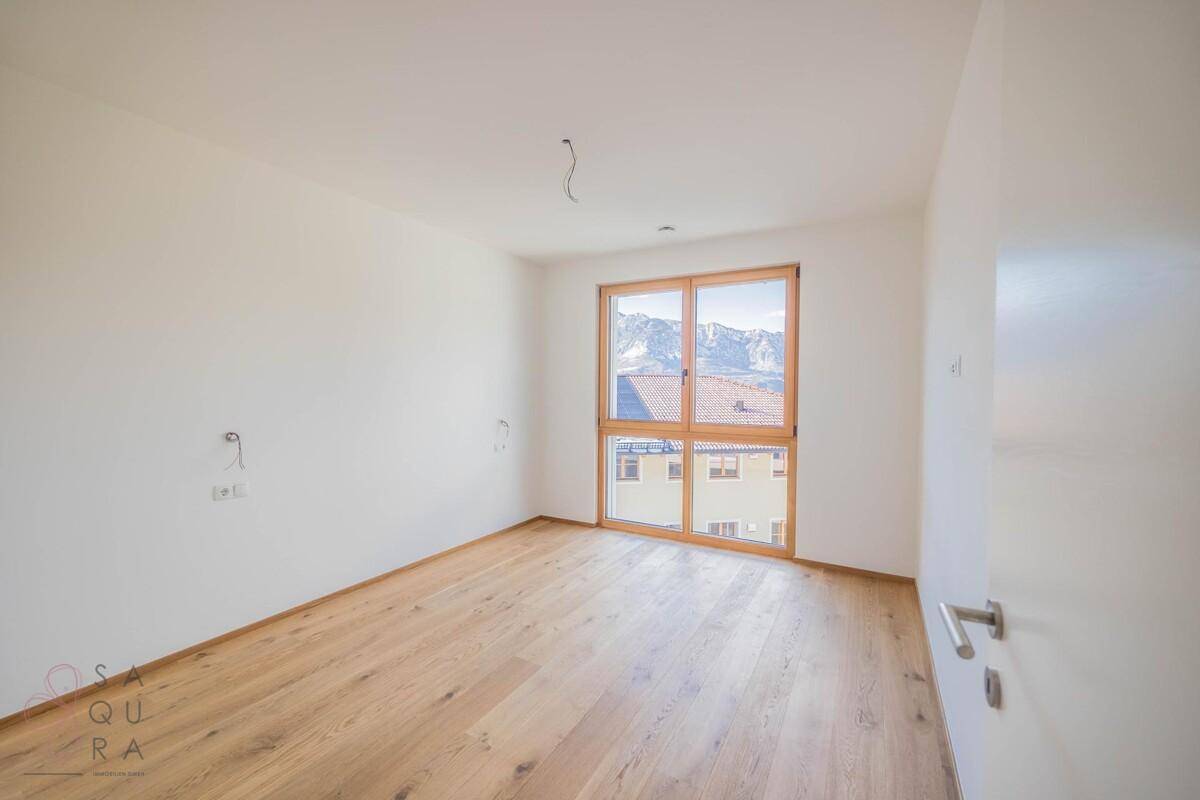 Helles Zimmer mit Holzboden und großem Fenster, das einen schönen Blick auf die Berge bietet.