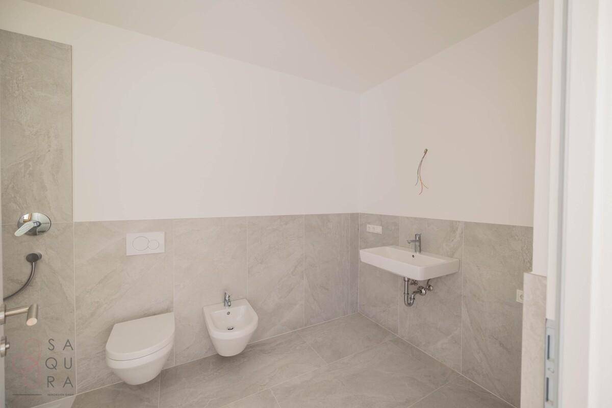 Zeitgemäßes Badezimmer mit grauen Fliesen, WC, Bidet und einem einzelnen Waschbecken.