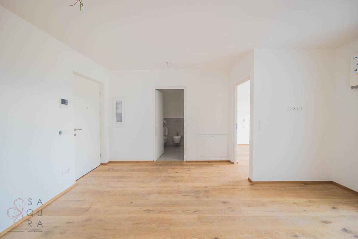 Unmöblierter Raum mit Holzboden und mehreren Türen, eine davon führt zu einem Badezimmer mit Bidet.