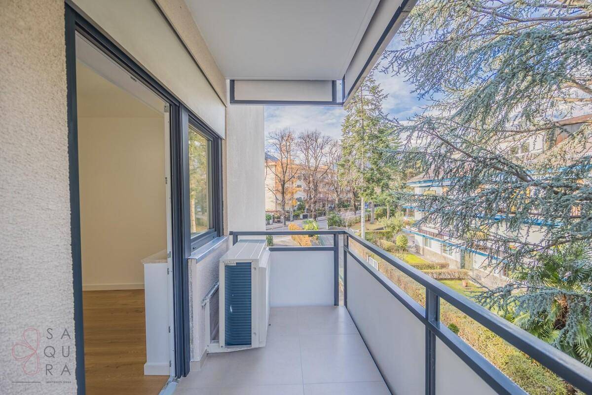 Kleiner Balkon mit Klimaanlage und Blick auf die grüne Umgebung und Nachbargebäude.
