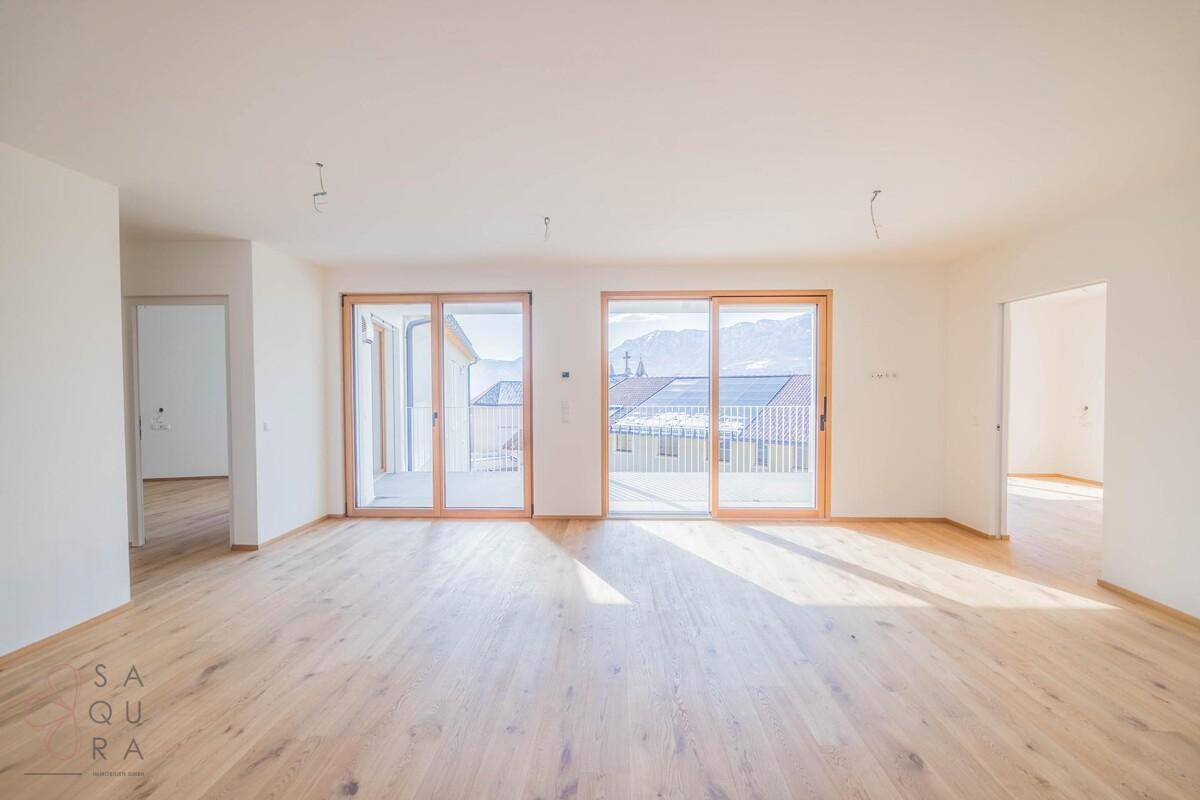 Geräumiges Wohnzimmer mit hellem Holzboden und großen Schiebetüren, die auf einen Balkon führen.