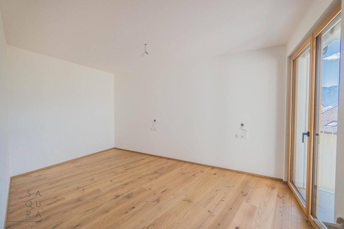 Unmöbliertes Schlafzimmer mit Holzboden und Zugang zu einem Balkon, ideal für viel Tageslicht.