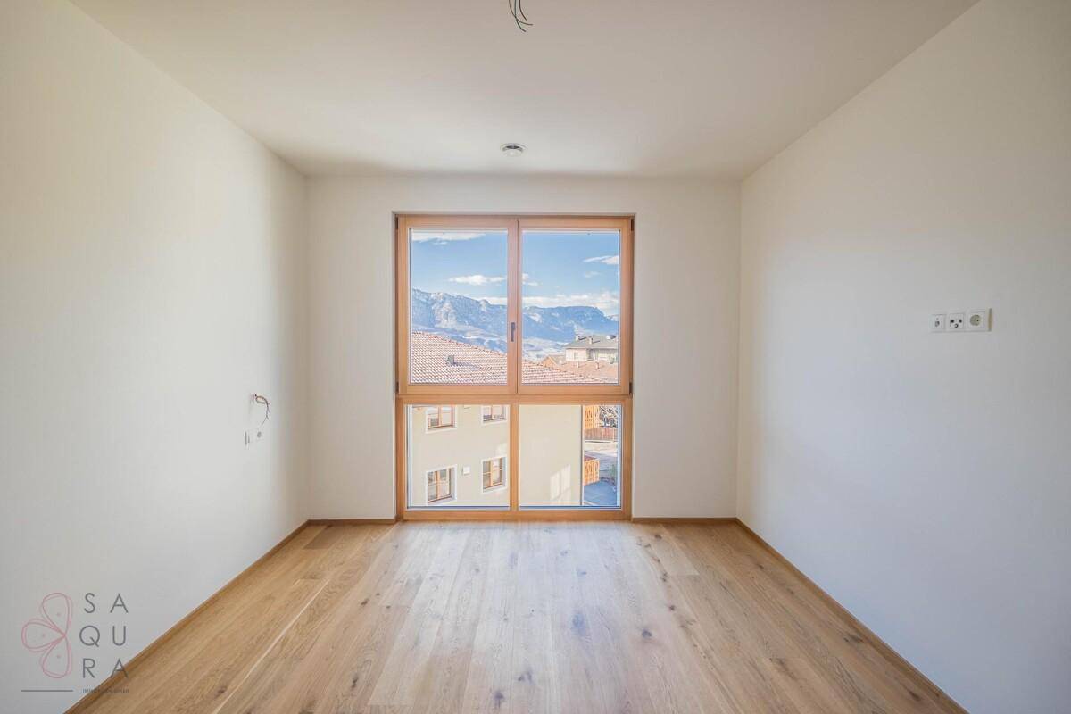 Lichtdurchflutetes Zimmer mit Holzboden und weitem Blick auf die schneebedeckten Berge.