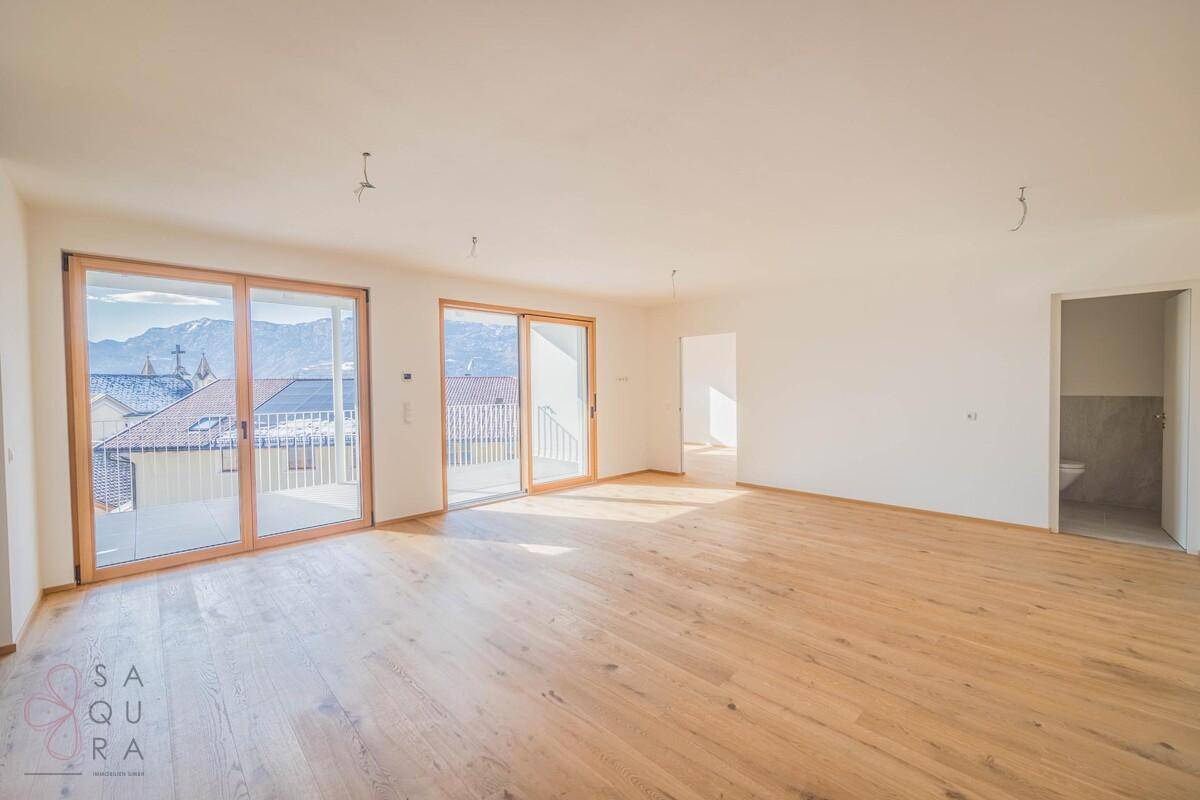 Lichtdurchfluteter Wohnbereich mit Holzboden und Blick auf die Berge durch die Balkontüren.