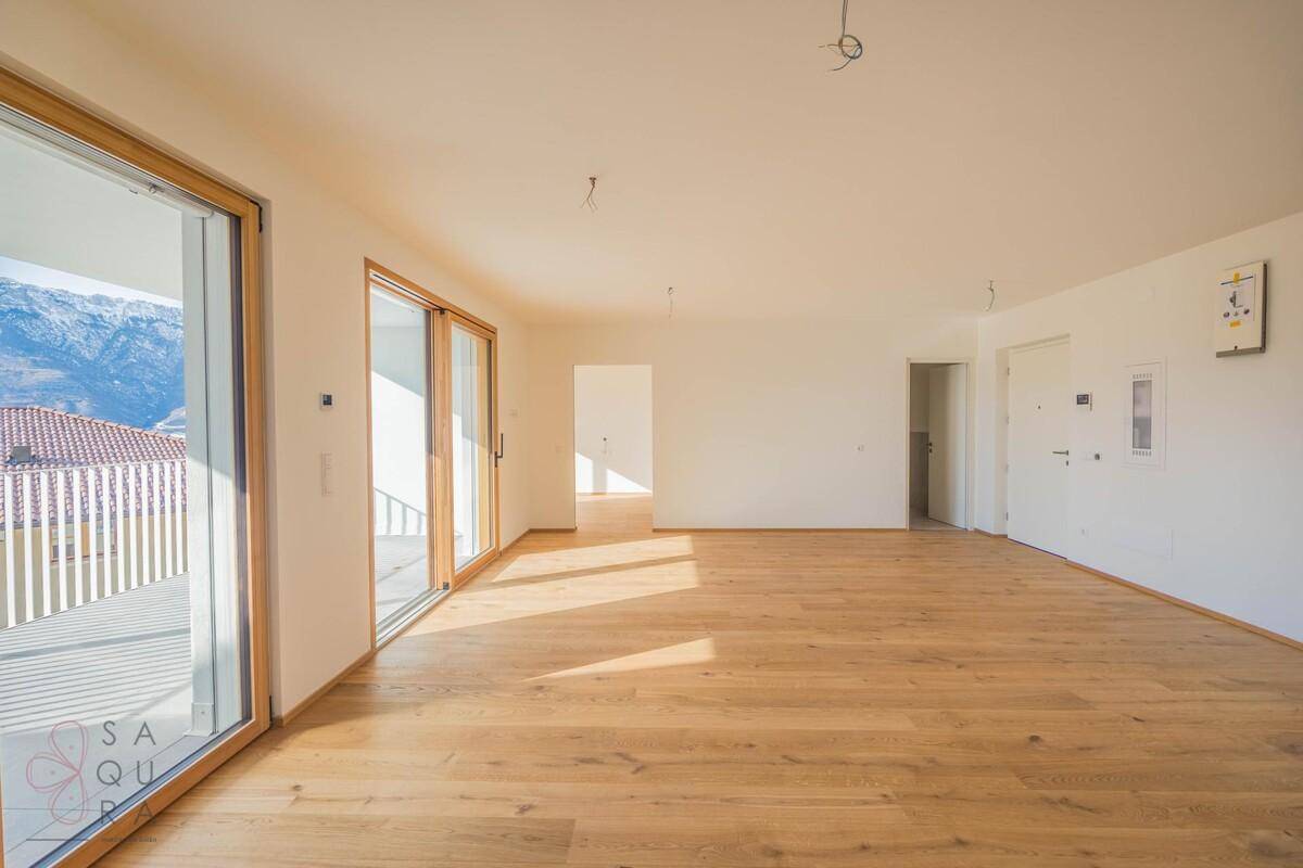 Großzügiger Wohnbereich mit Holzboden und Schiebetüren, die Zugang zu einem sonnigen Balkon bieten.