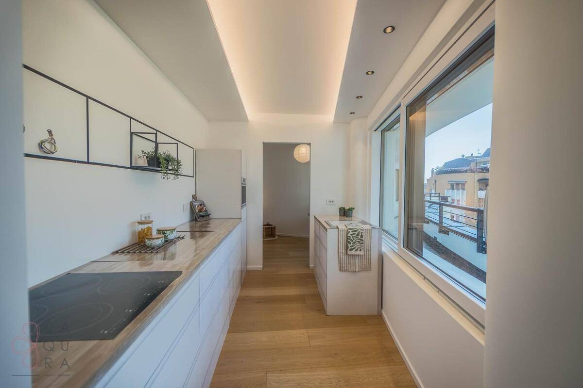 Moderne Küchenzeile mit weißen Schränken, Holzarbeitsplatte und großem Fenster mit Bergblick.
