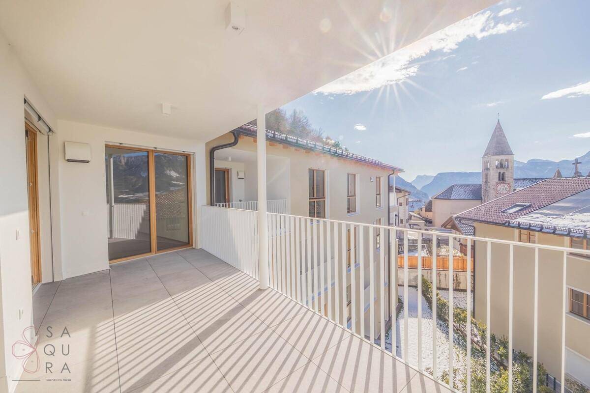 Sonniger Balkon mit Fliesenboden und Blick auf die umliegenden Gebäude und Berge.