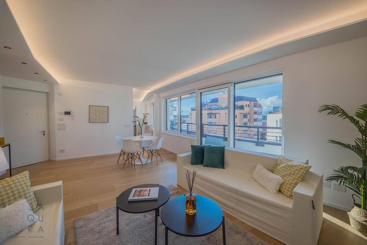 Heller Wohn- und Essbereich mit Holzboden, minimalistischer Einrichtung und Zugang zu einem Balkon.