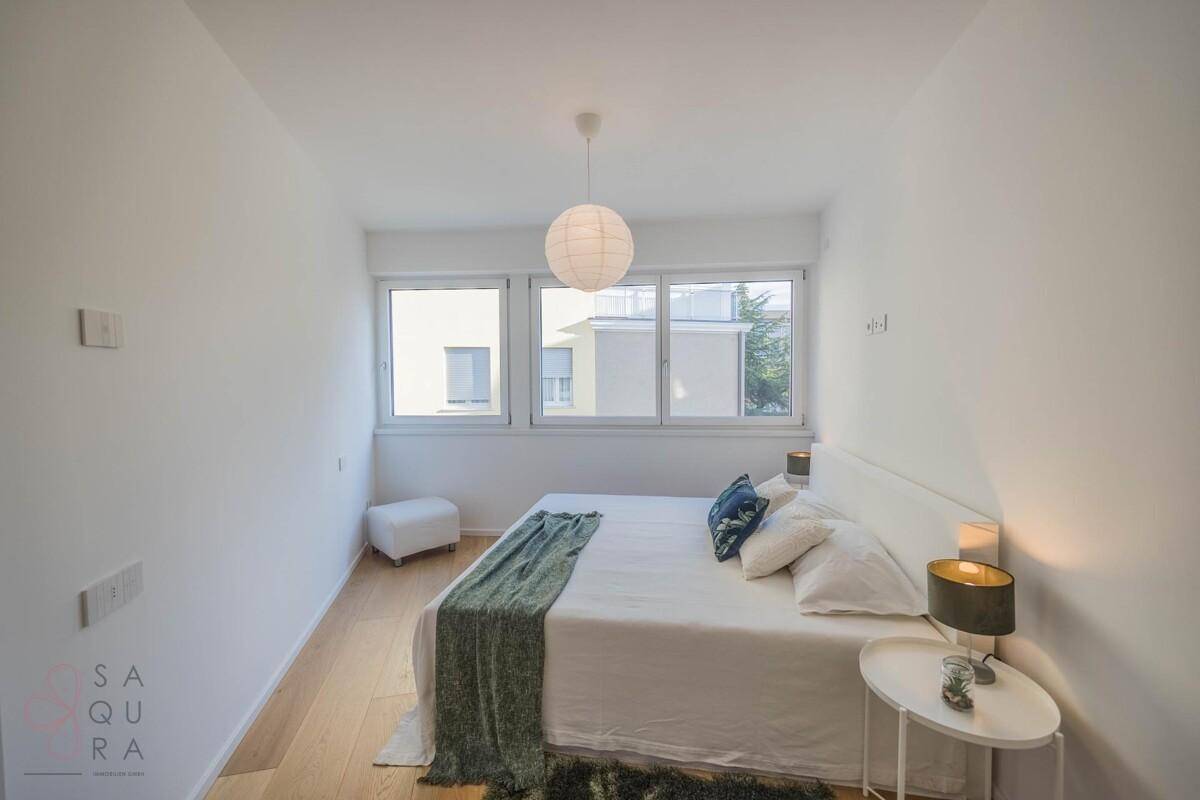 Modernes Schlafzimmer mit Doppelbett, Holzboden und großen Fenstern mit Stadtblick.