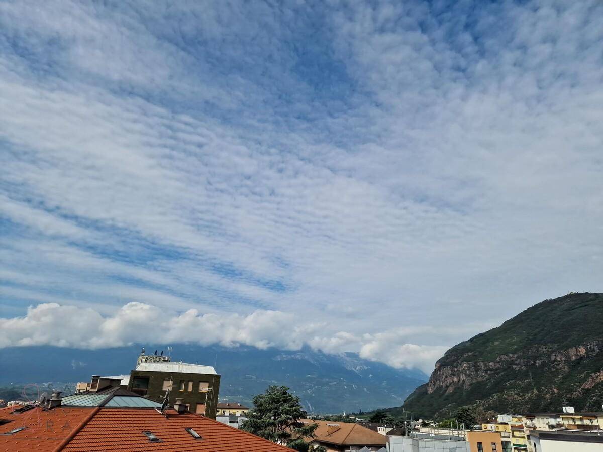 Weitläufiger Blick über die Dächer der Stadt mit Bergen im Hintergrund unter einem bewölkten Himmel.