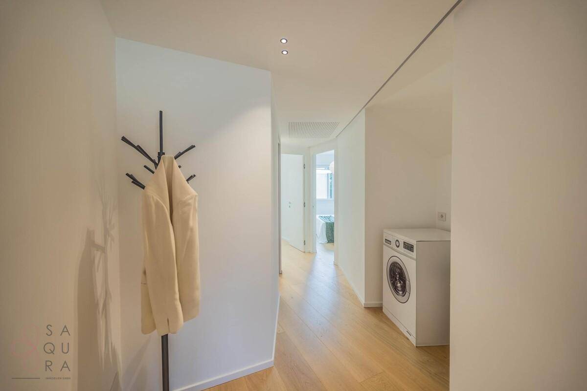 Heller Flur mit Holzboden, Garderobe und Waschmaschine, der zu weiteren Räumen führt.