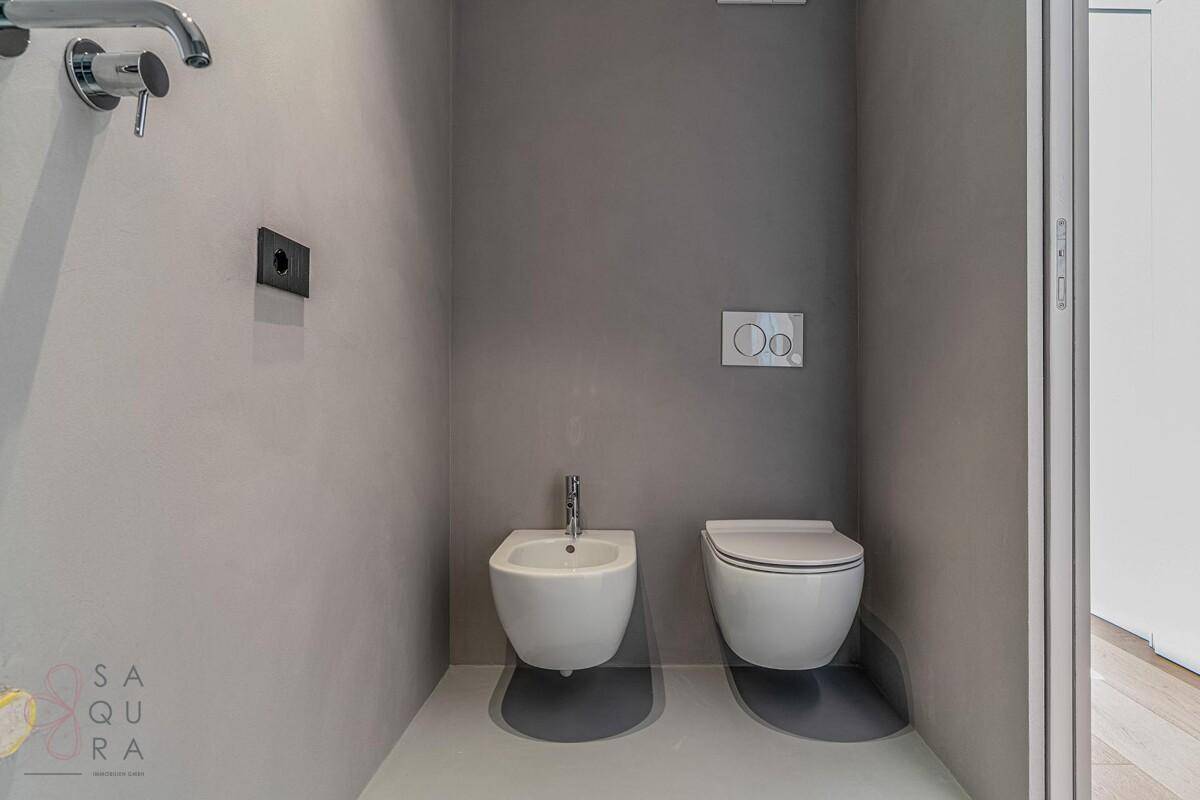 Modernes WC mit Bidet, wandhängender Toilette und grauen Wänden in minimalistischem Design.