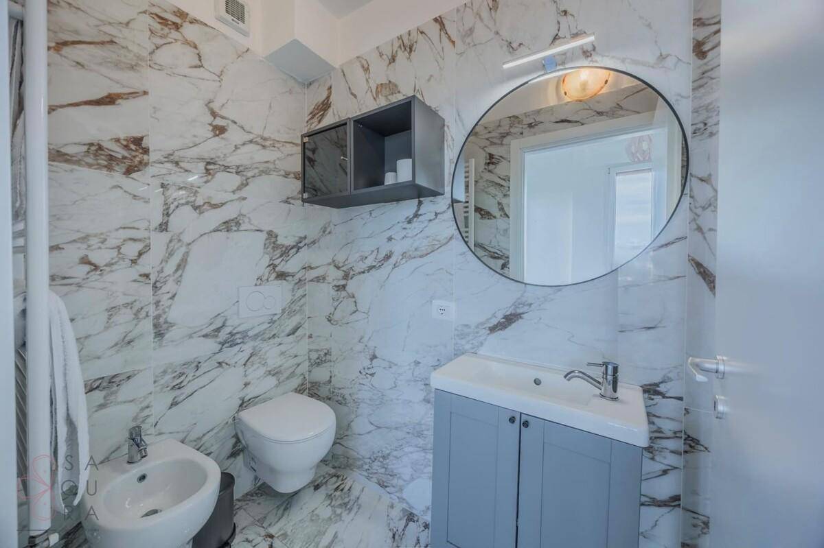 Elegantes Badezimmer mit Marmorfliesen, Waschtisch, Bidet und einem runden Spiegel.