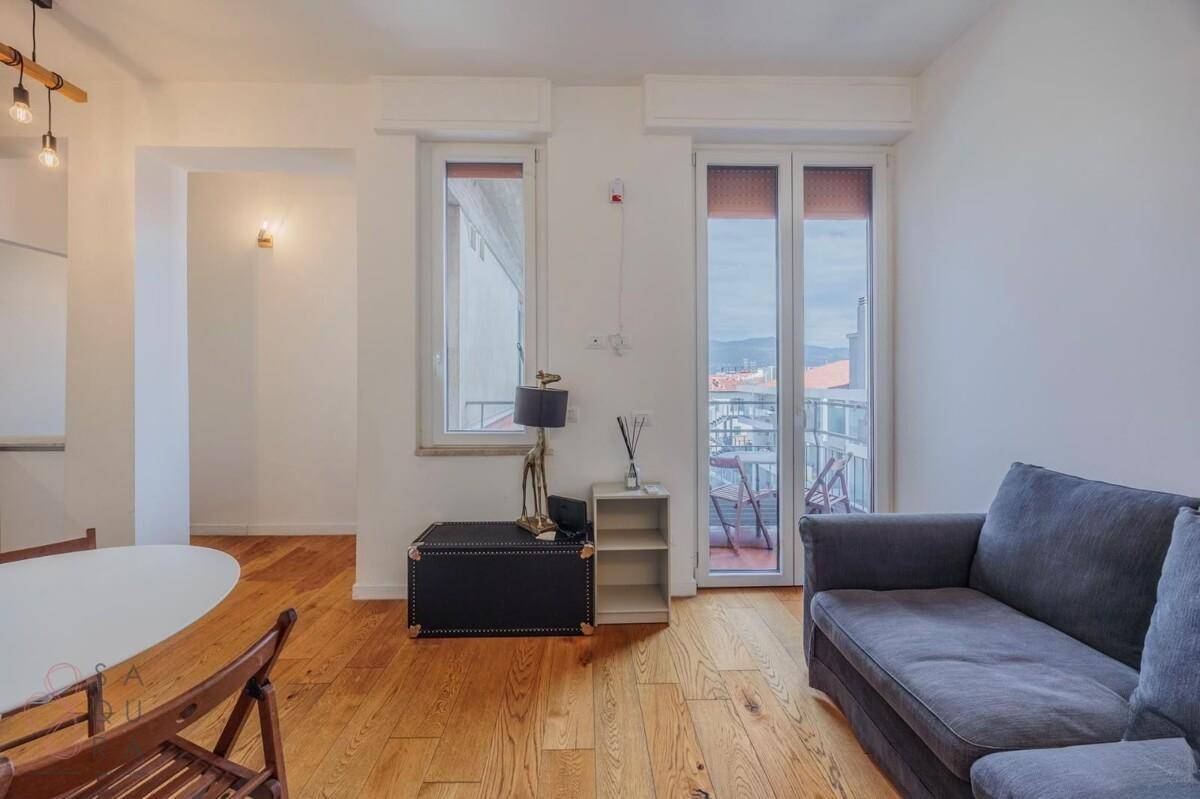 Gemütliches Wohnzimmer mit Holzboden und großen Fenstern, die Zugang zum Balkon bieten.
