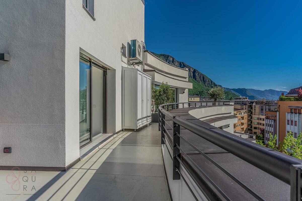 Langer, geschwungener Balkon mit moderner Brüstung und Blick auf die Stadt und Berge.
