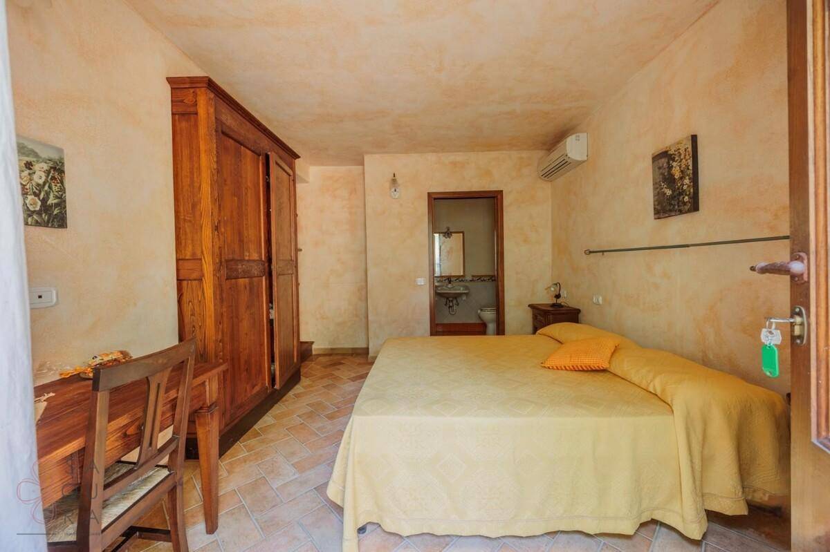 Schlafzimmer mit Holzkleiderschrank, Terrakottafliesen und direktem Zugang zum Badezimmer.