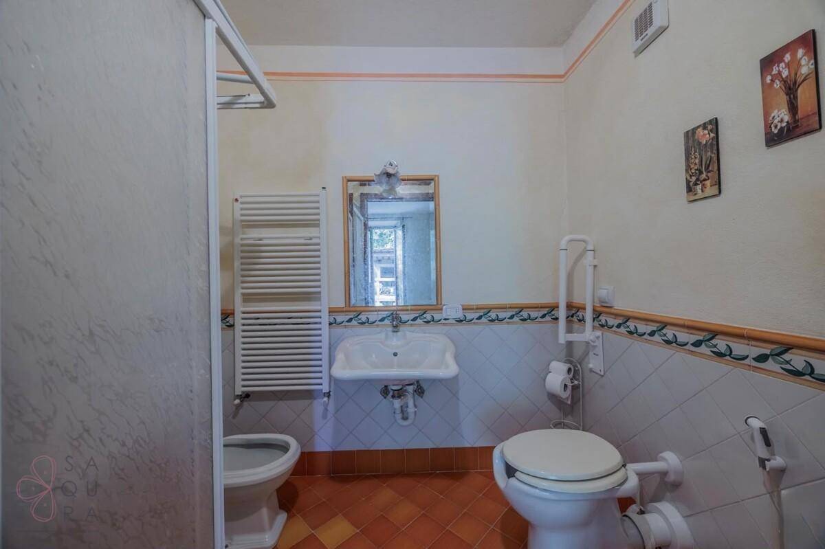 Funktionales Badezimmer mit Dusche, WC, Waschbecken und Heizkörper, ausgestattet mit Haltegriffen.