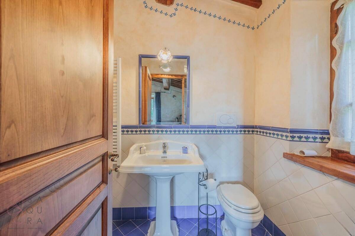 Badezimmer mit Standwaschbecken, WC und Spiegel, in traditionellem blau-weißem Design.