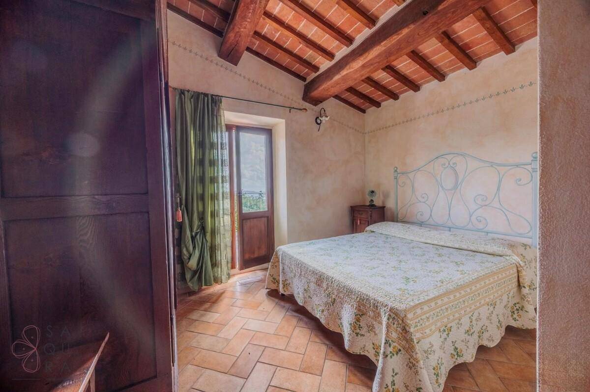 Helles Schlafzimmer mit Terrakottafliesen, Holzbalken und Zugang zu einem kleinen Balkon.