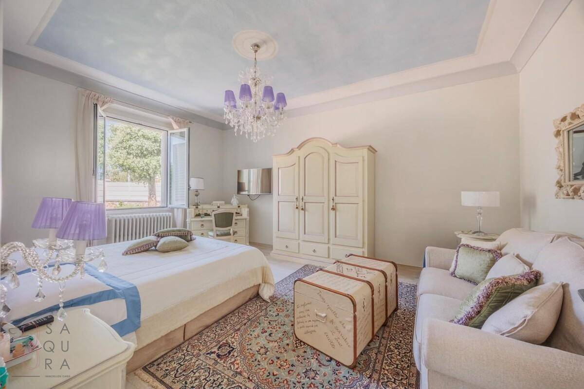 Geräumiges Schlafzimmer mit klassischem Mobiliar, Kronleuchter und Blick ins Grüne.