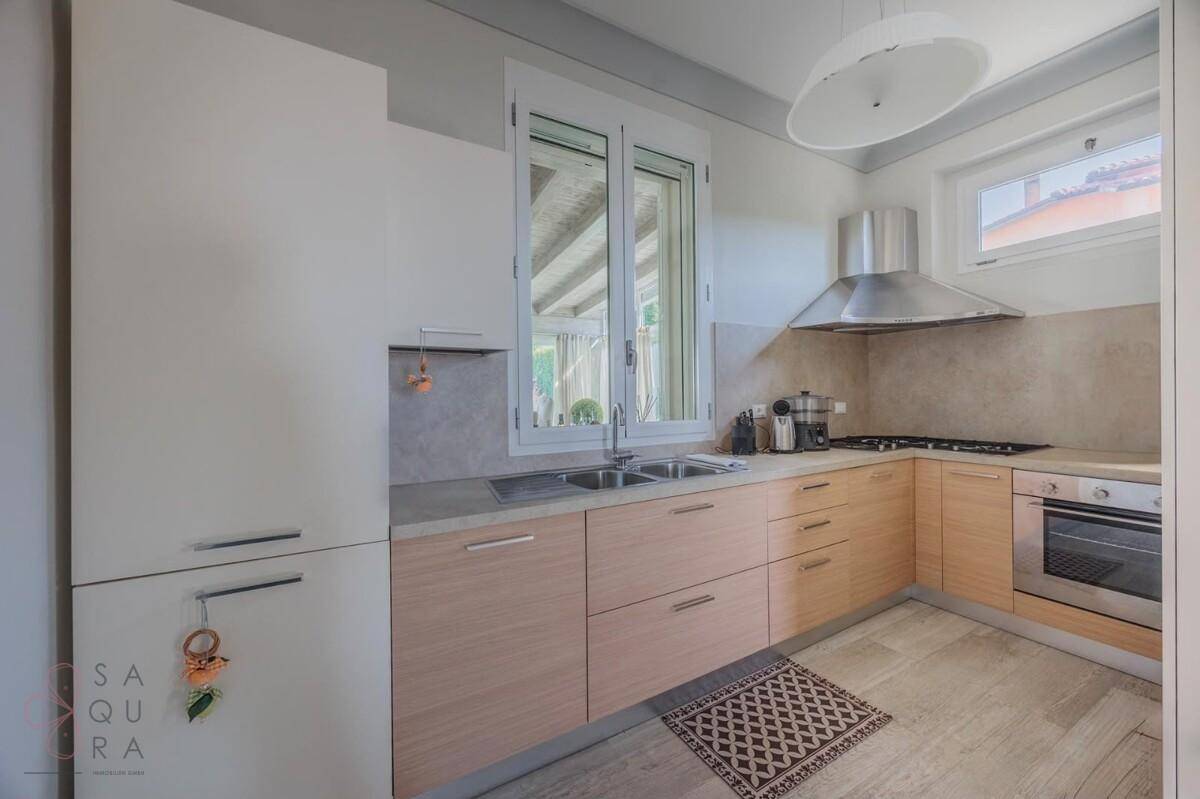 Moderne Küche mit hellen Holzfronten, Edelstahlgeräten und Fenster mit Blick ins Grüne.