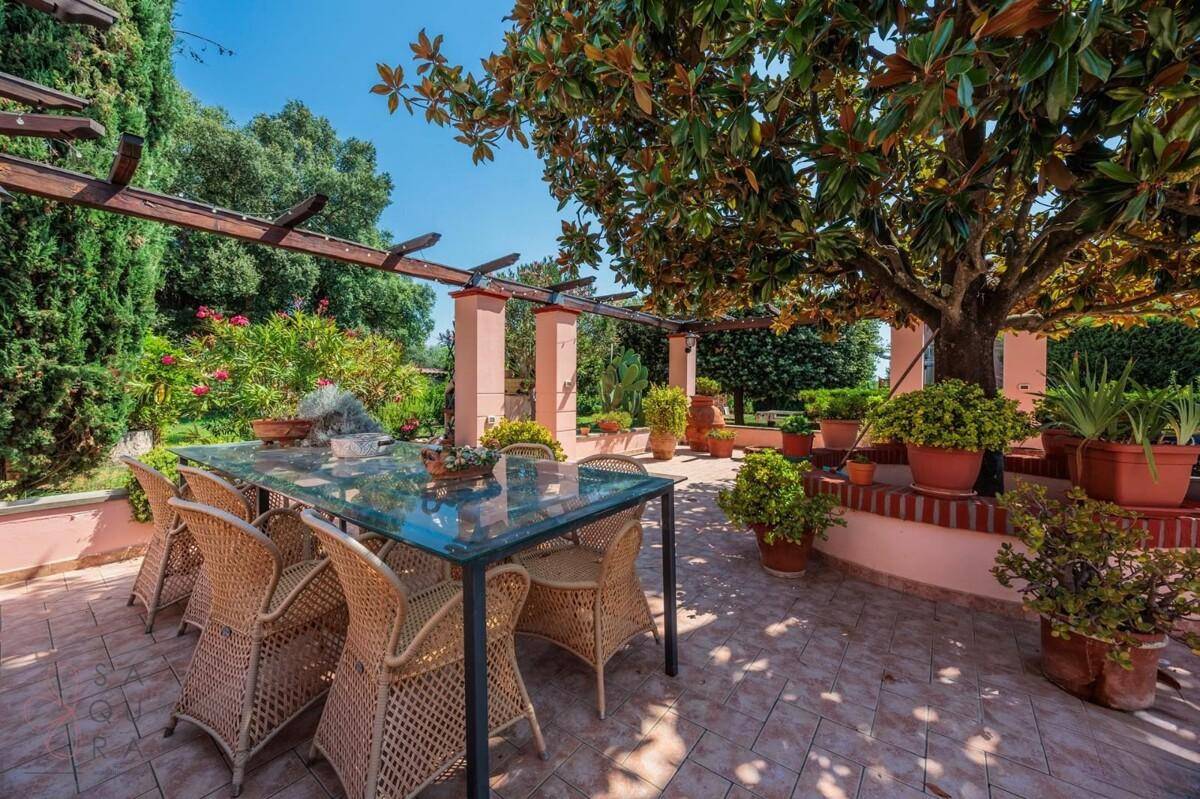 Gemütliche Terrasse mit großem Esstisch und Korbstühlen unter einer schattenspendenden Pergola im Garten.