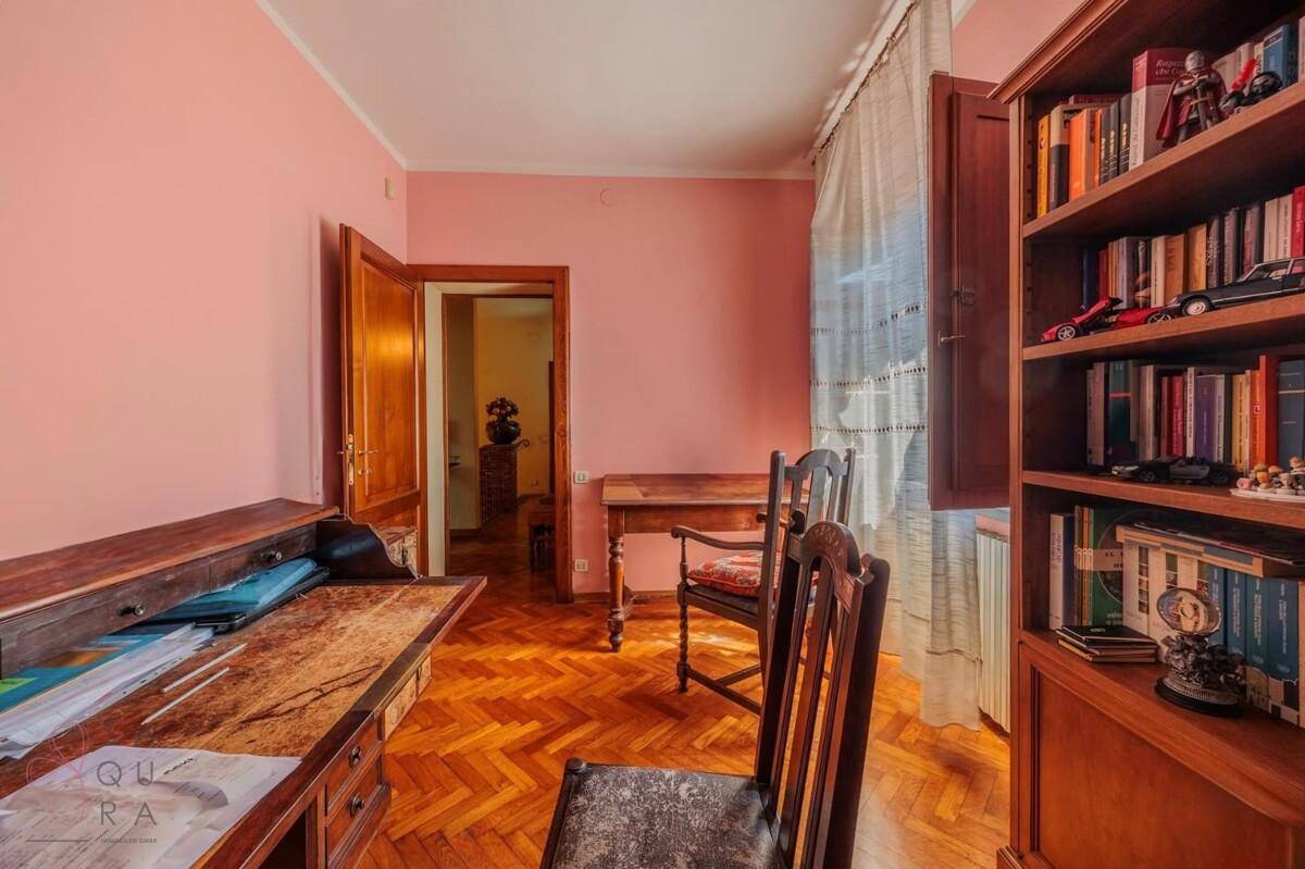 Helles Arbeitszimmer mit Fischgrätparkett, Holzmöbeln und einem Fenster mit Blick ins Grüne.