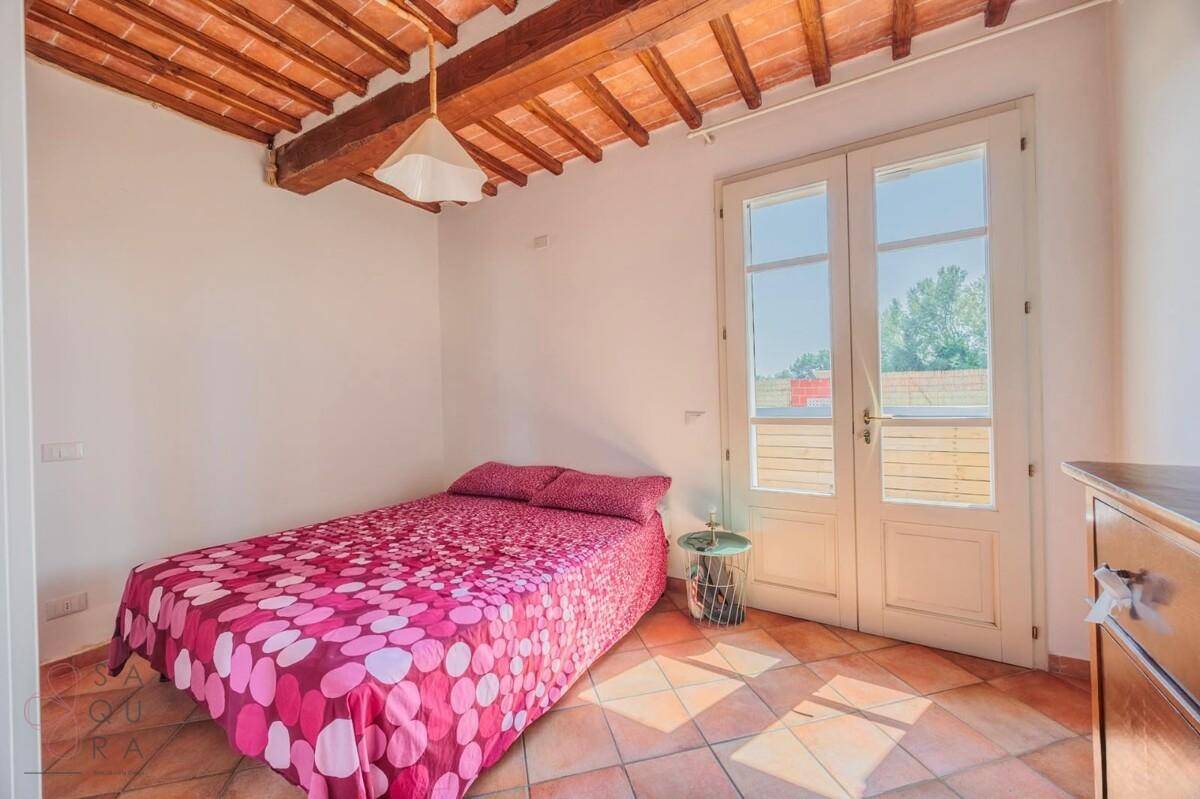 Schlafzimmer mit Terrakottaboden, Holzbalkendecke und französischen Türen, die viel Licht hereinlassen.