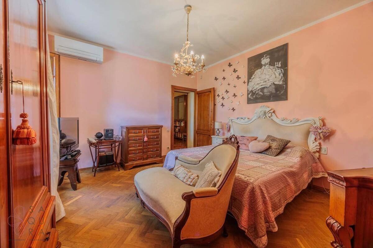 Elegantes Schlafzimmer mit Fischgrätparkett, rosa Wänden und einem opulenten Kronleuchter.