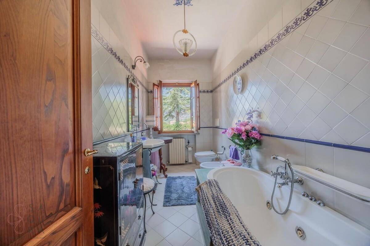 Geräumiges Badezimmer mit Badewanne, weißen Fliesen und einem Fenster mit Blick ins Grüne.
