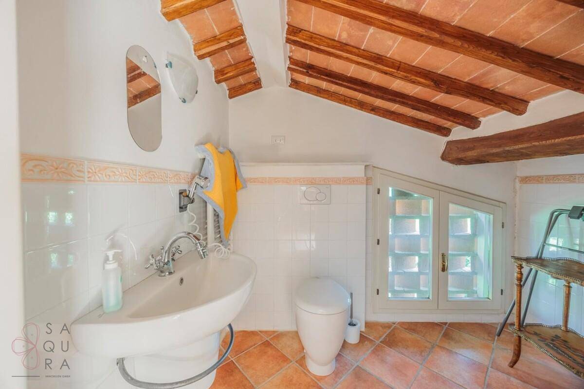 Dachbadezimmer mit Terrakottaboden, freiliegenden Holzbalken und einem Waschbecken.