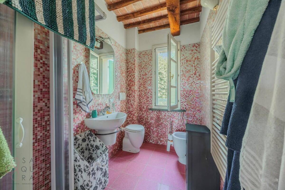 Farbenfrohes Badezimmer mit rosa Mosaikfliesen, Terrakottaboden und einem Fenster für Tageslicht.