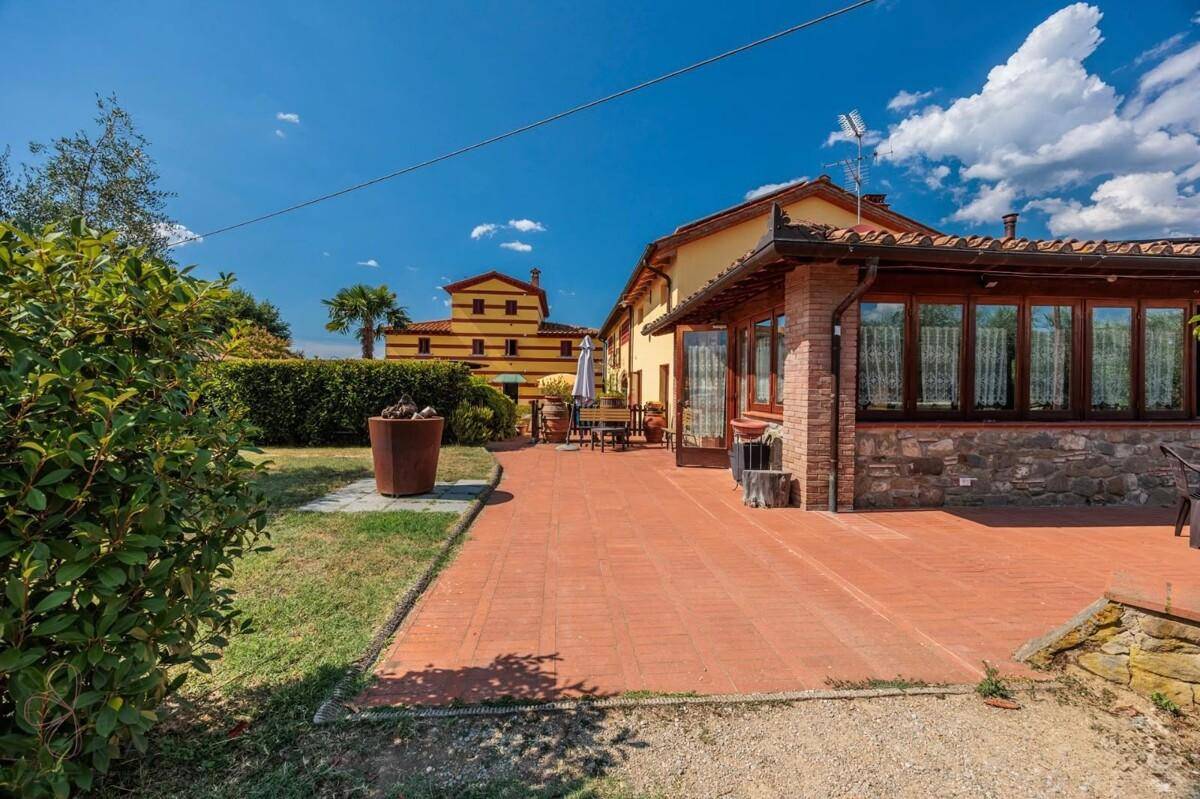 Gepflasterte Terrasse mit Zugang zum Garten, umgeben von grünen Hecken und mediterraner Vegetation.