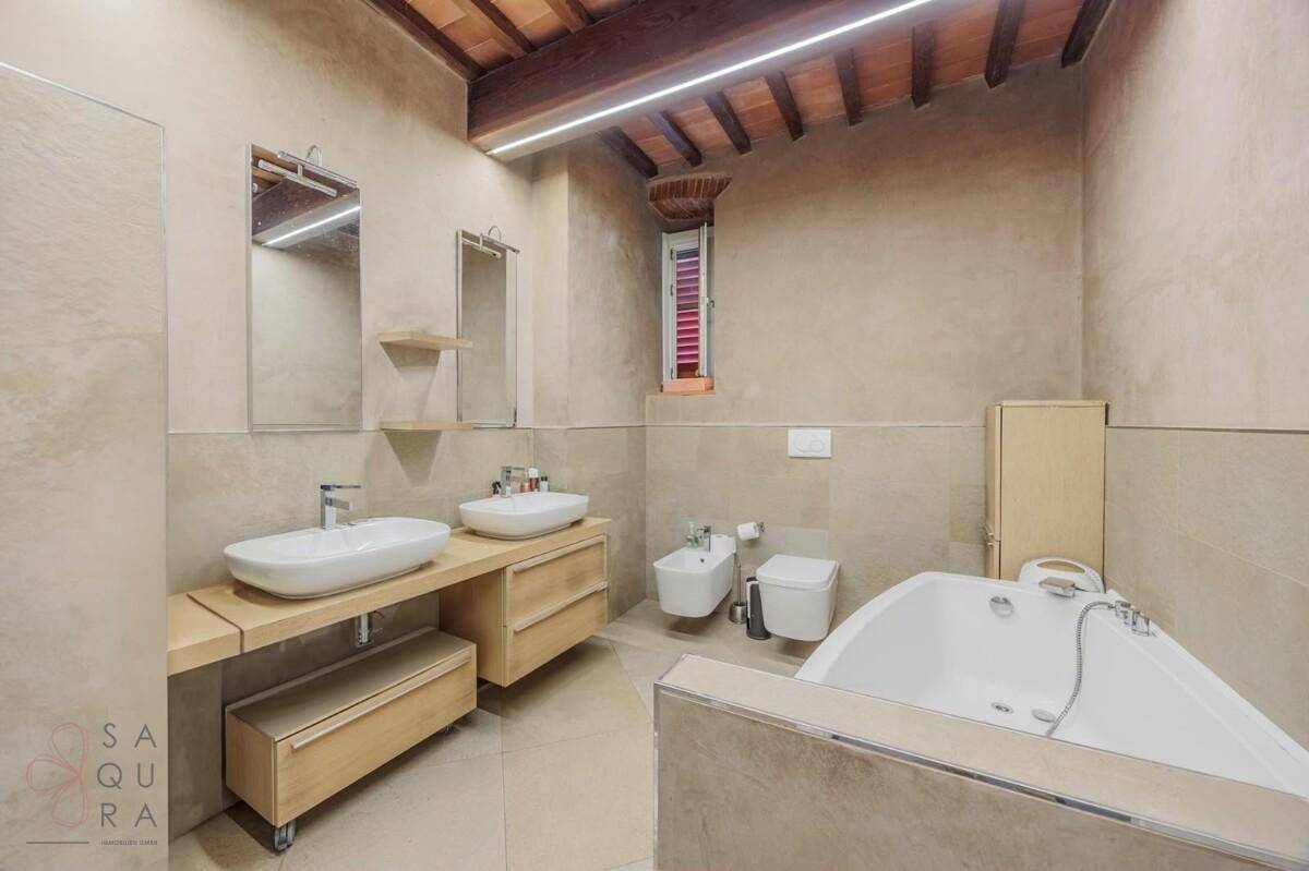 Modernes Badezimmer mit Doppelwaschbecken, Bidet und Eckbadewanne unter Holzbalkendecke.