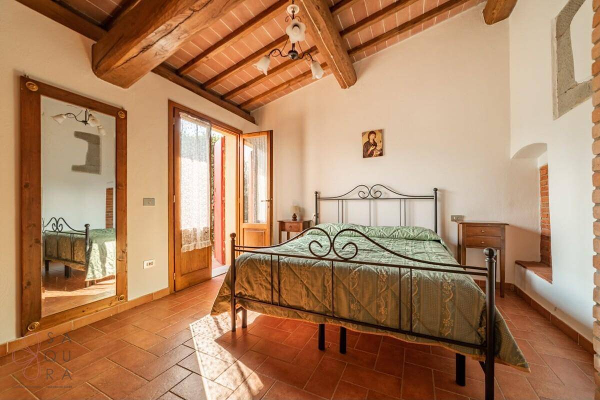 Geräumiges Schlafzimmer mit schmiedeeisernem Bett, Holzbalkendecke und Zugang zum Außenbereich.