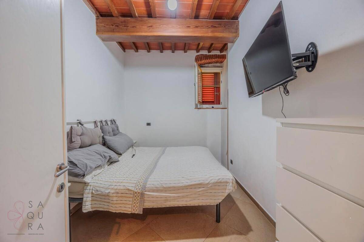 Kleines Schlafzimmer mit Doppelbett, Wandfernseher und rustikaler Holzbalkendecke.