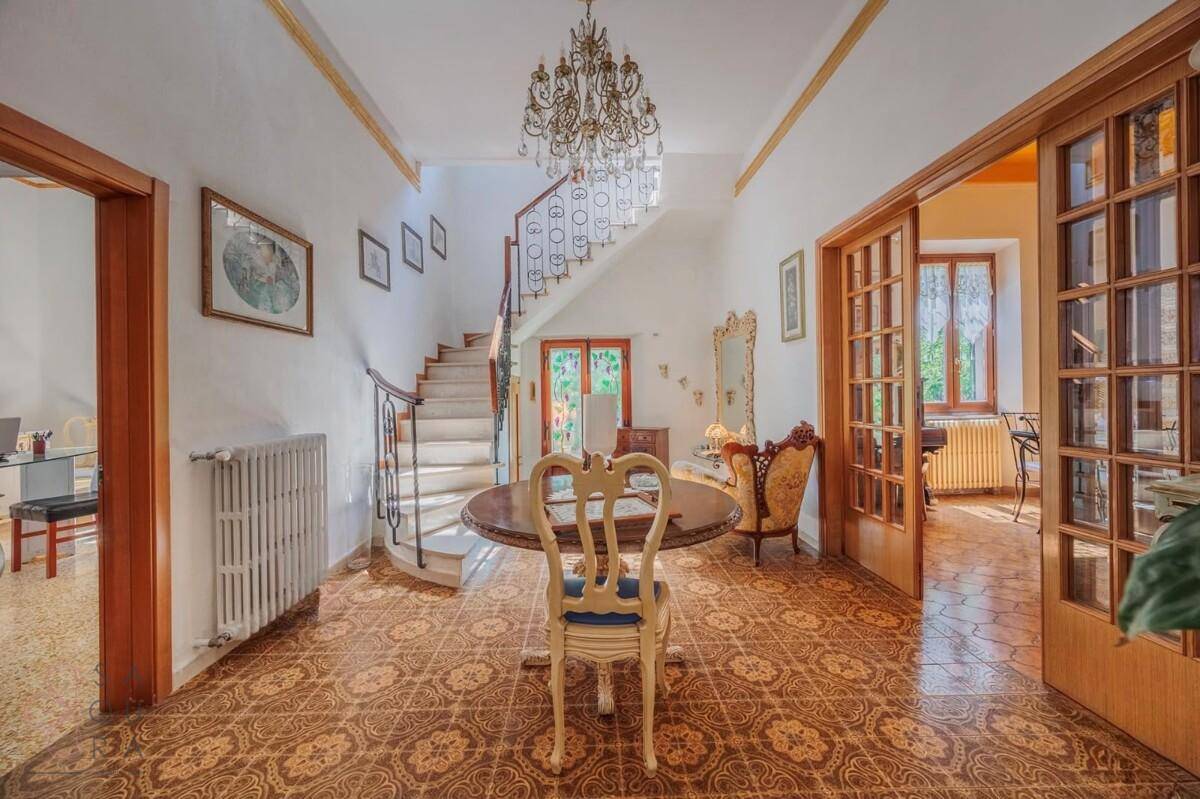Geräumiger Eingangsbereich mit geschwungener Treppe, Kronleuchter und gemustertem Fliesenboden.
