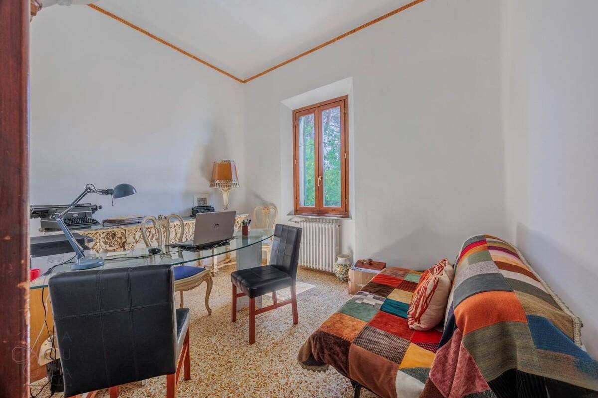 Helles Arbeitszimmer mit Schreibtisch, Stühlen und einem bunten Tagesbett am Fenster.