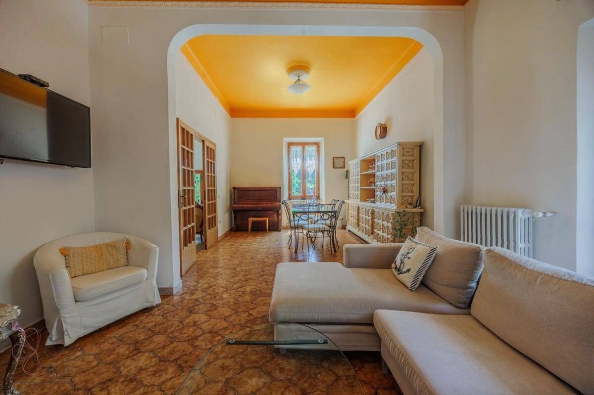 Gemütliches Wohnzimmer mit beiger Couch, gemustertem Fliesenboden und einem Essbereich im Hintergrund.
