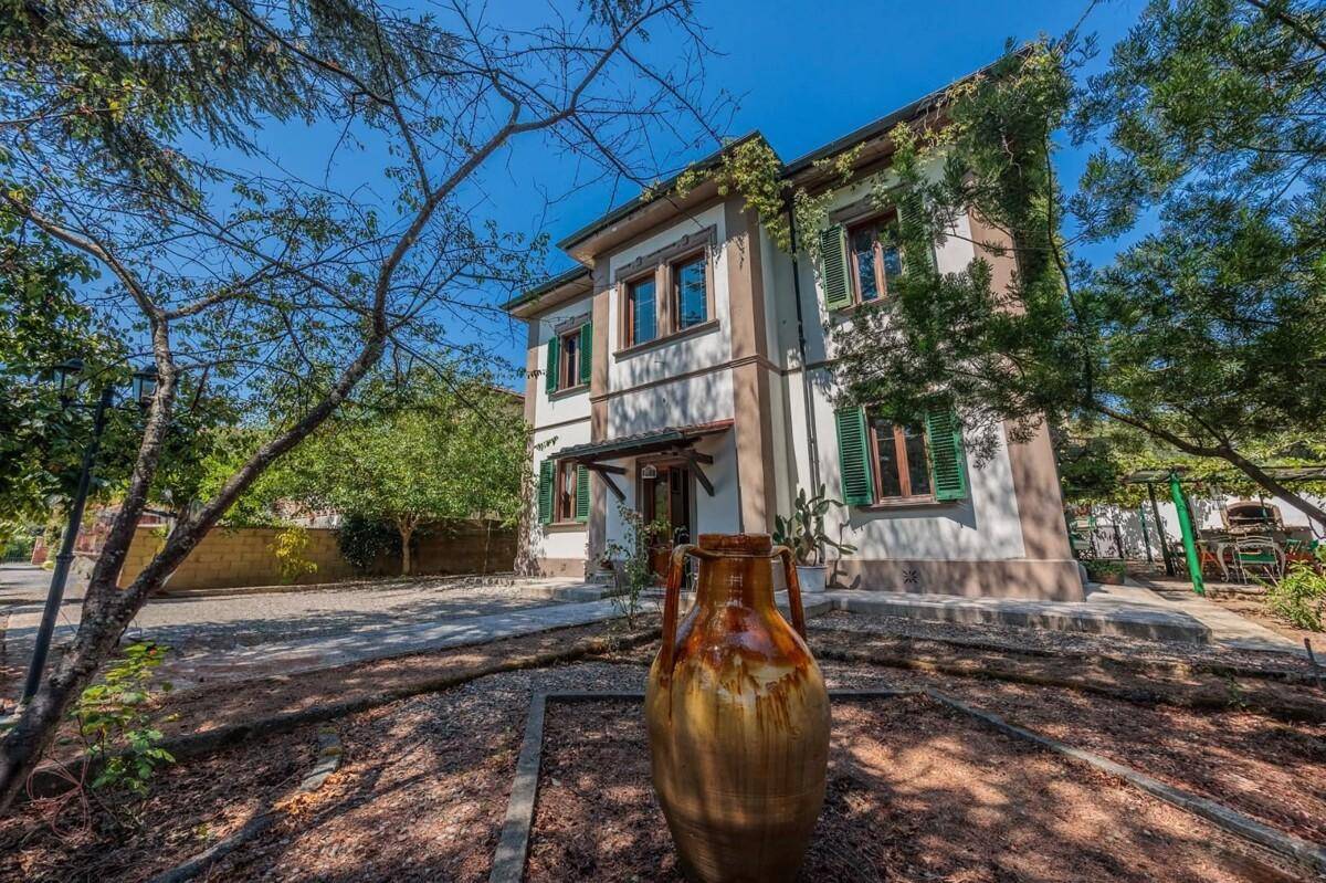 Seitlicher Blick auf das Haus mit mediterranem Garten und dekorativer Amphore im Vordergrund.