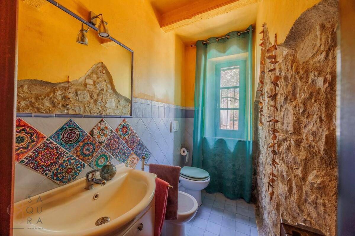 Farbenfrohes Badezimmer mit gemusterten Fliesen und Steinwand, ausgestattet mit Bidet und Fenster.