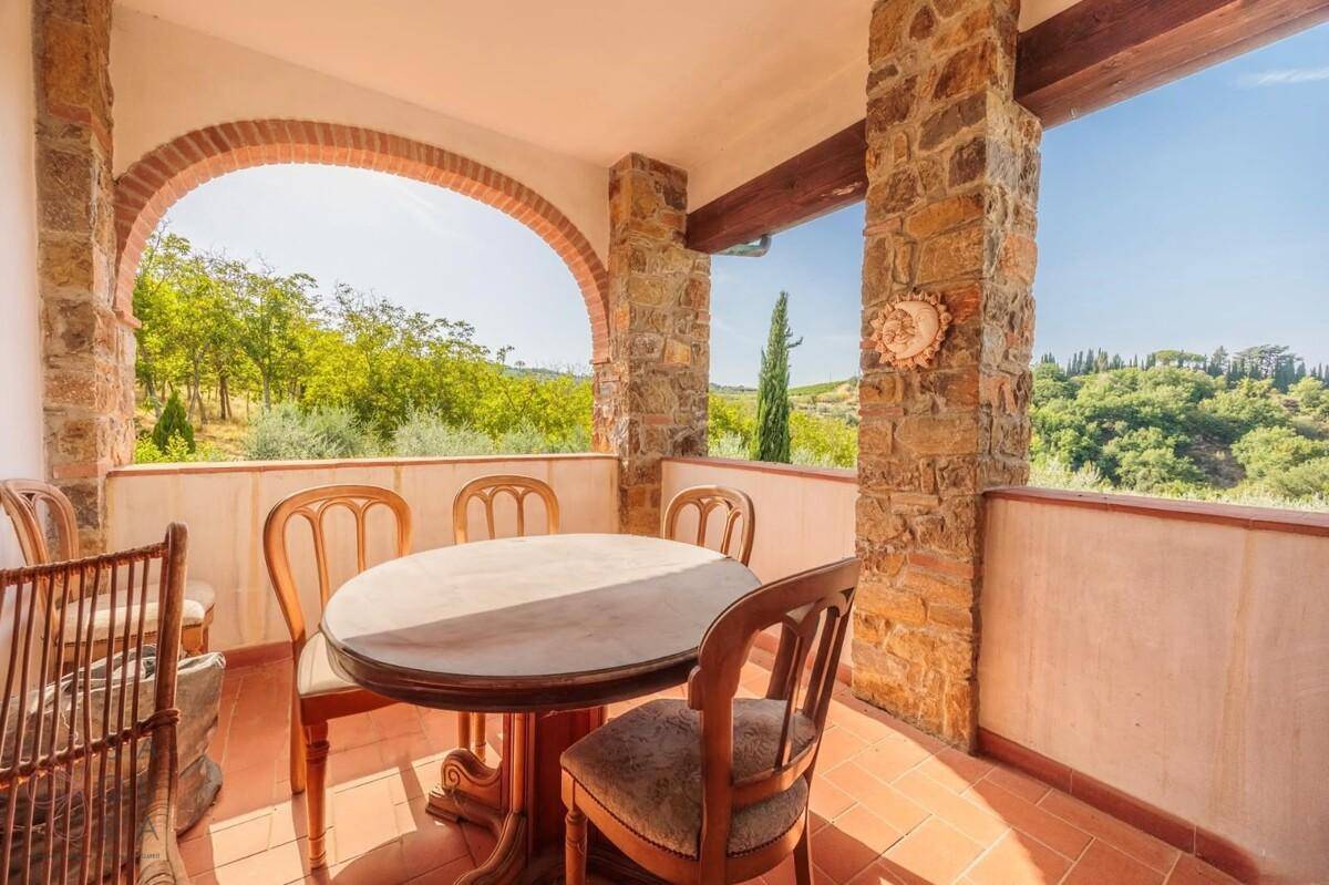 Überdachter Balkon mit Steinsäulen, Holztisch und Stühlen, bietet einen malerischen Blick auf die grüne Landschaft.
