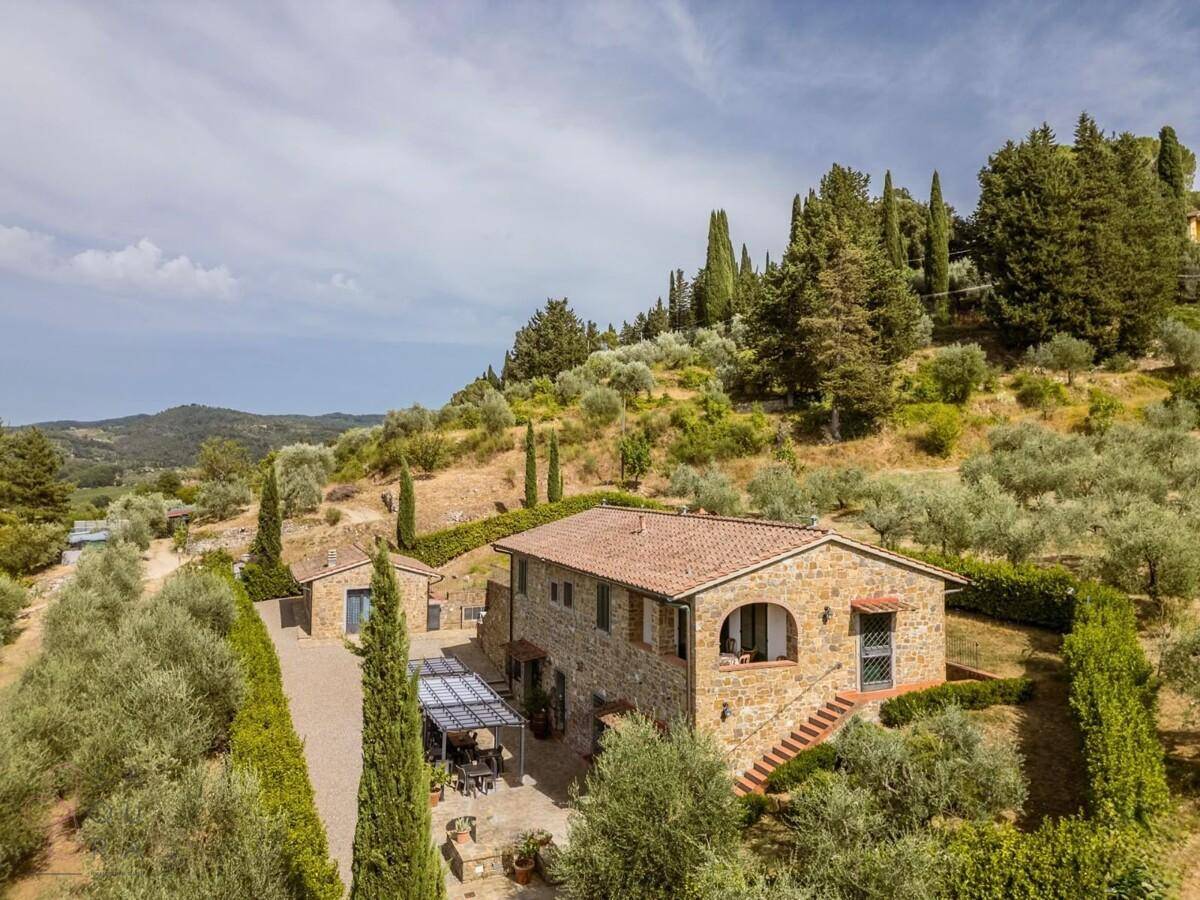 Weitläufige Ansicht des Landhauses mit Steinfassade, umgeben von üppiger mediterraner Vegetation und Olivenbäumen.