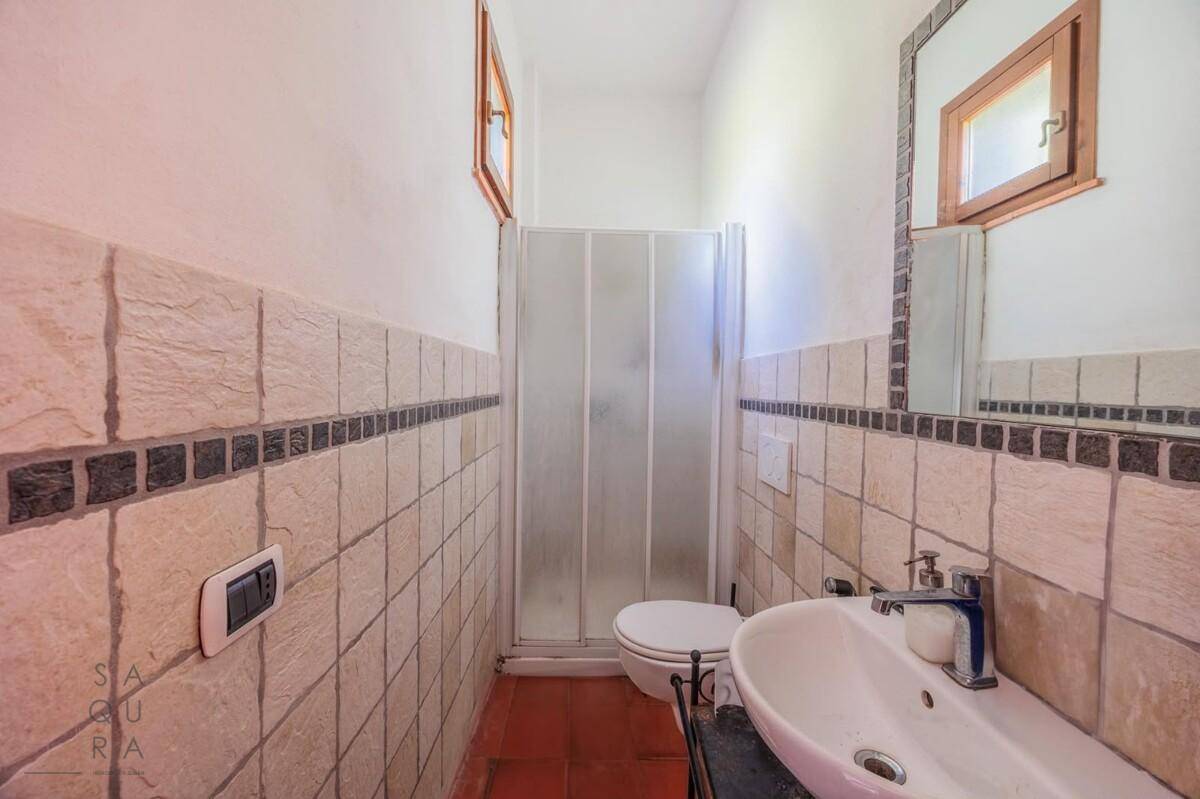 Kleines Badezimmer mit Duschkabine, WC und Einzelwaschbecken, gefliest mit beigen und schwarzen Fliesen.